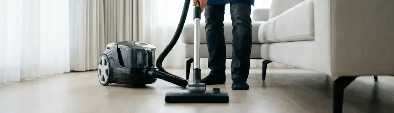 Professional house cleaner vacuuming a living room floor with a canister vacuum cleaner, Salt Lake City, UT.
