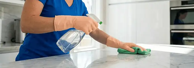 Maid service worker spraying and wiping a kitchen countertop with a microfiber cloth for sanitizing, Salt Lake City, UT.