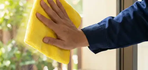 House cleaner wiping a glass window with a yellow microfiber cloth for streak-free cleaning, Salt Lake City, UT.